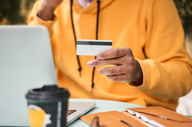 Man holding up a credit card next to a laptop